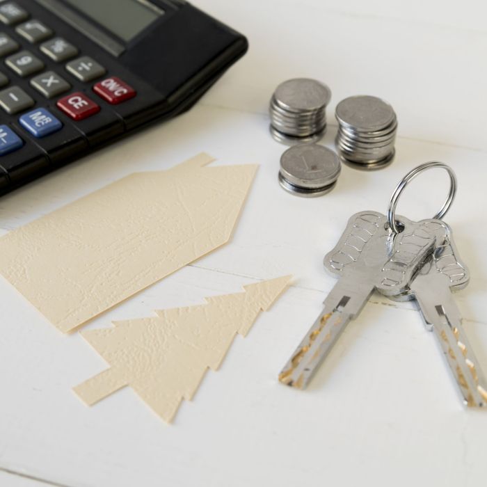 calculator-coins-stack-keys-with-house-tree-paper-cutout-white-wooden-table
